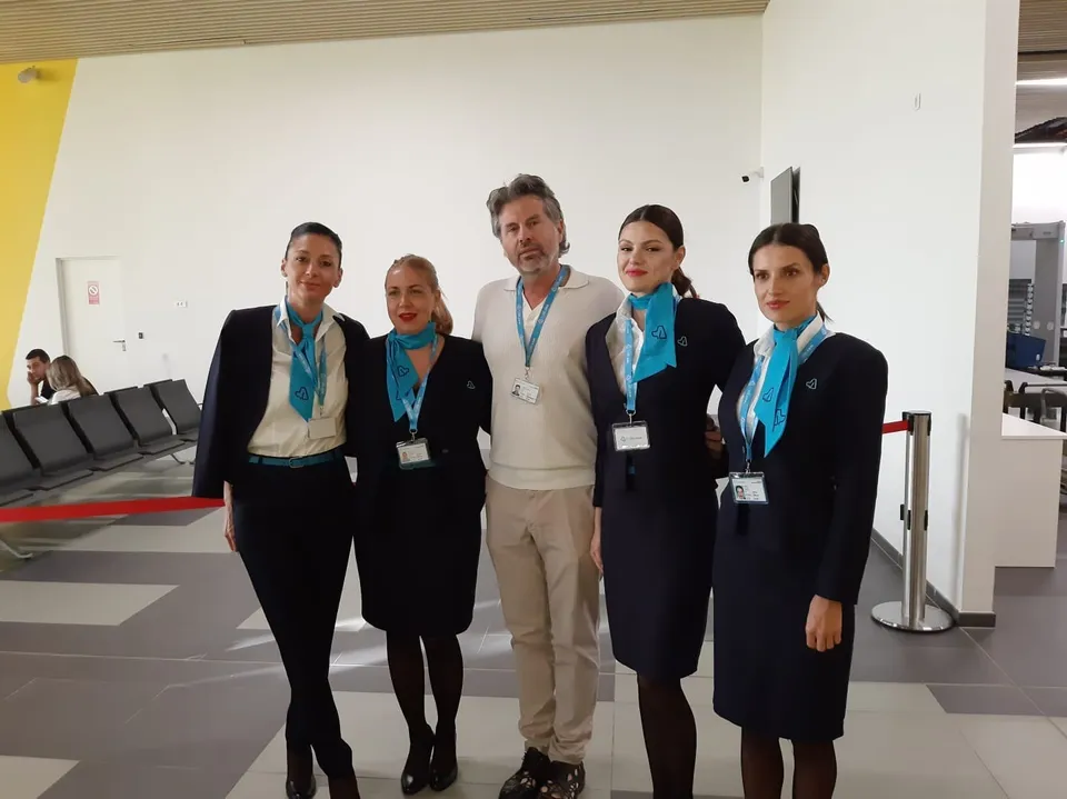 Cinci persoane, dintre care patru femei în uniforme de culoare închisă cu accesorii albastre, stau în picioare într-o încăpere cu pereți albi.