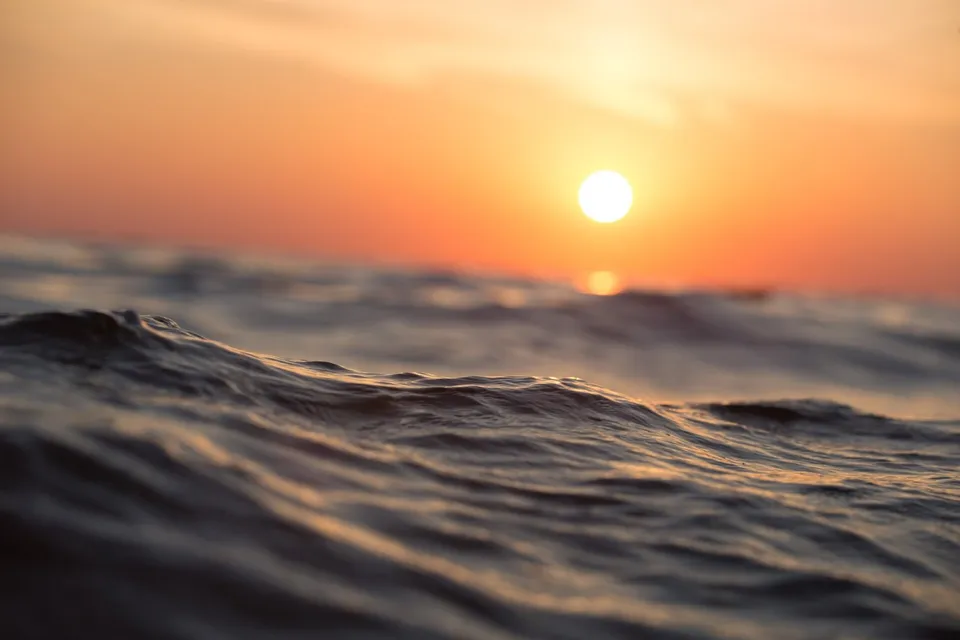 Soarele apune peste apele agitate ale unui ocean sub un cer portocaliu.