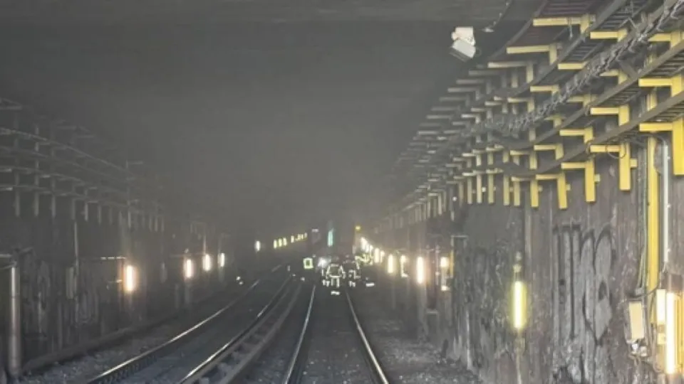 O vedere de la nivelul căilor ferate într-un tunel întunecat cu margini gri și structuri metalice galbene pe partea dreaptă.