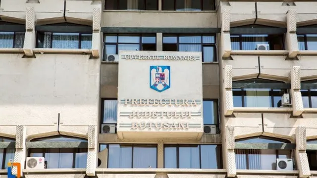 O clădire oficială cu un panou mare pe care scrie Prefectura Județului Botoșani, având un stema albastru și roșu în centru.