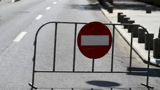 Un gard metalic cu un semn circular roșu și o bară albă este poziționat pe marginea unei străzi asfaltate.