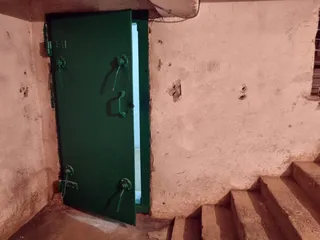O ușă metalică verde este deschisă într-un perete de beton lângă niște trepte de piatră.