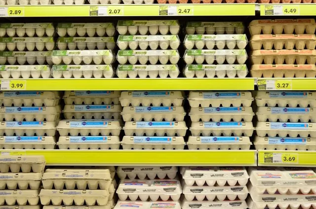 Mai multe rânduri de cutii de carton cu ou sunt așezate pe rafturi de supermarket cu etichete de preț galbene.