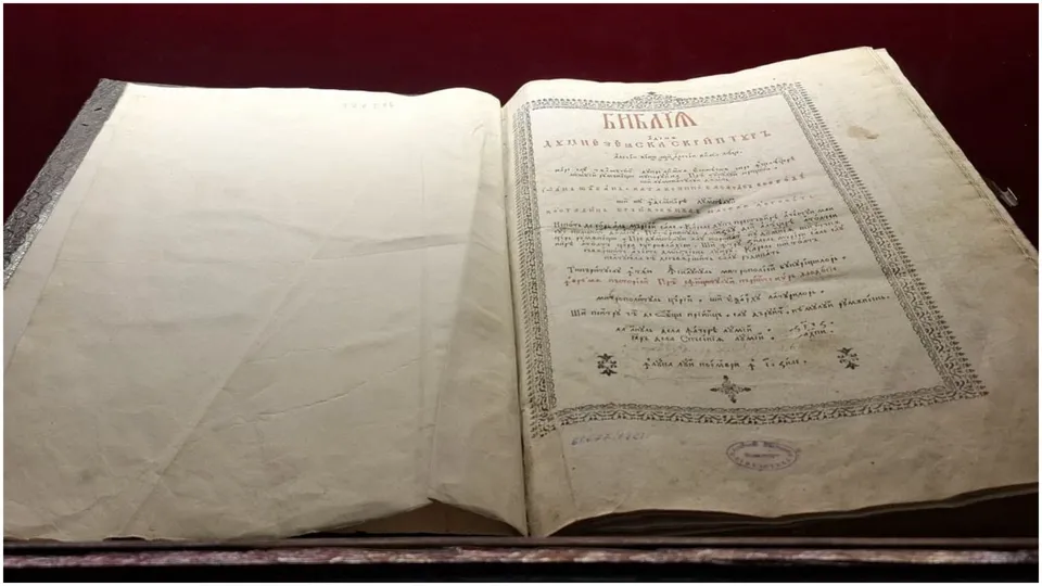 O carte veche deschisă prezintă pagini de hârtie îngălbenită cu text scris și margini decorate cu modele geometrice și florale.