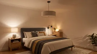 Un pat cu lenjerie albă și un comodin cu lampă stau într-o cameră cu un plafonier central și un copac într-un ghiveci.