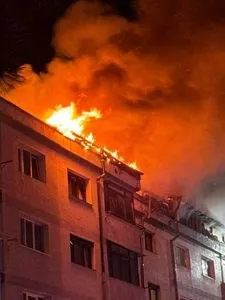 Flăcări mari și fum dens ies de pe acoperișul unei clădiri de locuințe pe timp de noapte.