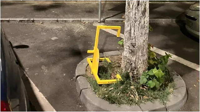 Un blocator de parcare galben este instalat pe un trotuar lângă un copac și un bord curb.