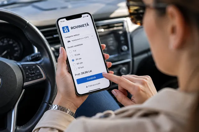 O persoană ține un telefon mobil în interiorul unui autoturism, afișând pe ecran un meniu de plată pentru rovinietă cu diverse opțiuni de durată.