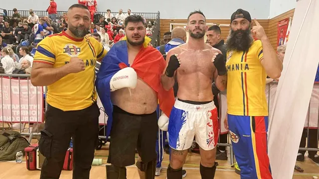 Patru bărbați stau în picioare într-o sală de sport, doi purtând tricouri galbene și doi fiind torți sau sportivi cu echipament de luptă.