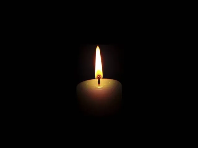 O lumânare aprinsă arde într-un mediu întunecat.