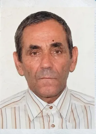 Un bărbat cu părul scurt și gri poartă o cămașă cu dungi verticale subțiri pe un fundal alb simplu.
