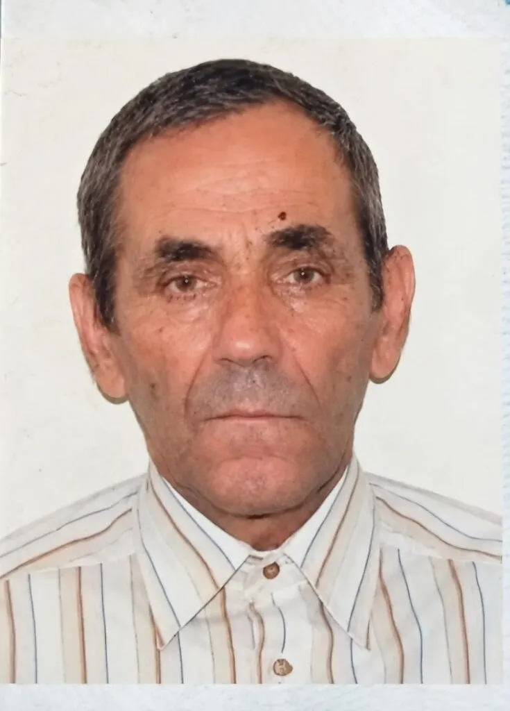 Un bărbat cu părul scurt și gri poartă o cămașă cu dungi verticale subțiri pe un fundal alb simplu.