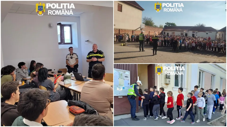 Un grup de persoane stă la mese într-o încăpere, în timp ce doi bărbați stau în picioare în fața lor.