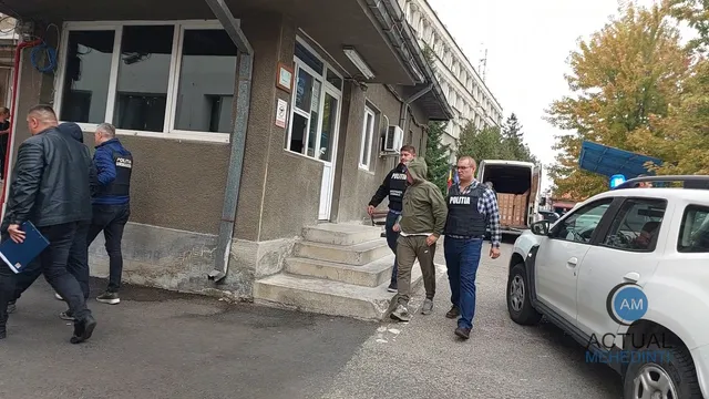 Cinci bărbați merg pe un trotuar lângă o clădire și o mașină albă, în timp ce un agent de poliție stă lângă un vehicul.