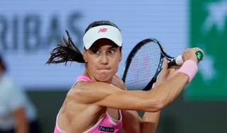 O tenismenă cu părul legat, purând o vizoră albă și tricou roz, este prinsă în mișcare while loveând cu racheta într-un meci de tenis.