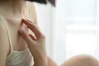 O persoană cu părul negru își atinge zona claviculară și a umărului cu mâna dreaptă.
