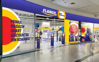 Fațada unui magazin Flanco cu panouri albastre, galbene și roșii, situat într-un spațiu comercial cu podea lucioasă și vitrine mari de sticlă.