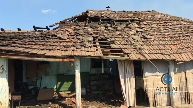 O casă cu acoperiș din țiglă parțial distrus și structuri de lemn expuse sub un cer senin.