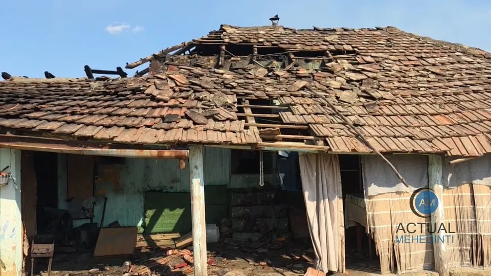 O casă cu acoperiș din țiglă parțial distrus și structuri de lemn expuse sub un cer senin.