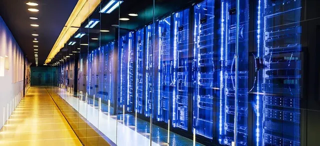 Rânduri de rack-uri de servere cu lumini albastre sunt amplasate într-un coridor lung și îngust cu podea lucioasă și tavan iluminat.
