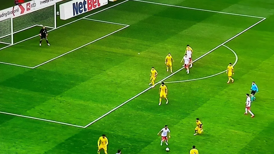 Jucători de fotbal în echipamente galbene și albe sunt pe un teren de fotbal verde sub lumini artificiale.