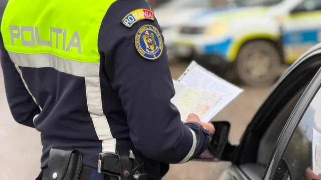 Un polițist în uniformă cu inscripția POLITIA și emblema ROMANIA ține documente lângă o mașină neagră, având un vehicul de serviciu în fundal.
