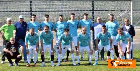 O echipă de fotbaliști îmbrăcați în echipamente albastre și albe pozează într-un grup pe un teren de fotbal verde.