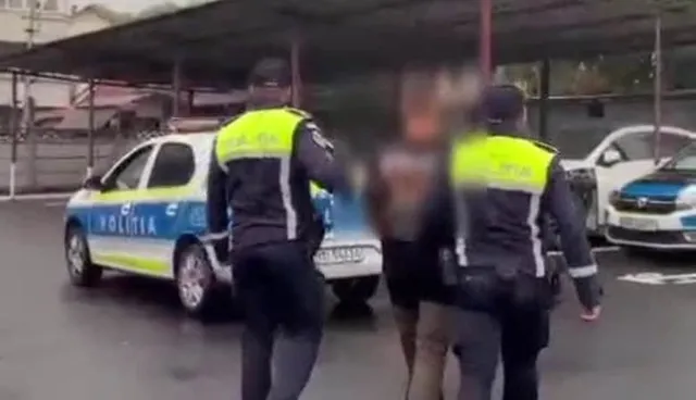 Unii polițiști în uniformă cu veste reflectorizante verzi stau lângă o mașină de poliție albastră și albă și un bărbat cu fața neclară.