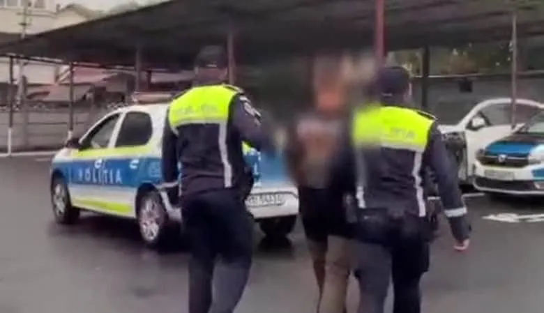 Unii polițiști în uniformă cu veste reflectorizante verzi stau lângă o mașină de poliție albastră și albă și un bărbat cu fața neclară.