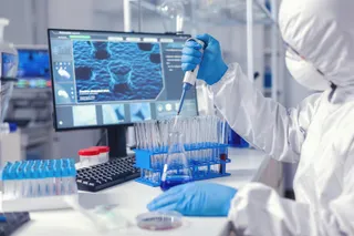 O persoană îmbrăcată într-un costum alb de protecție și mănuși albastre folosește un pipetă pentru a transfera un lichid într-un recipient de laborator.