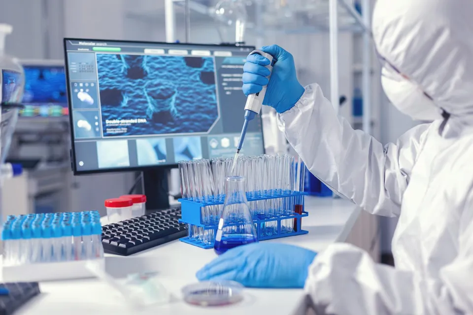 O persoană îmbrăcată într-un costum alb de protecție și mănuși albastre folosește un pipetă pentru a transfera un lichid într-un recipient de laborator.