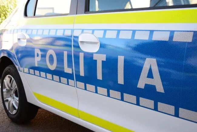 Imaginea arată lateralul unei mașini albe, albastre și galbene, cu inscripția „POLIȚIA” pe ușă.