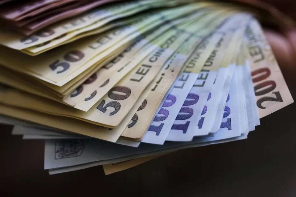 Un evantai de bancnote de lei românești cu valori de cincizeci, o sută și două sute de lei este întins pe o suprafață plană.