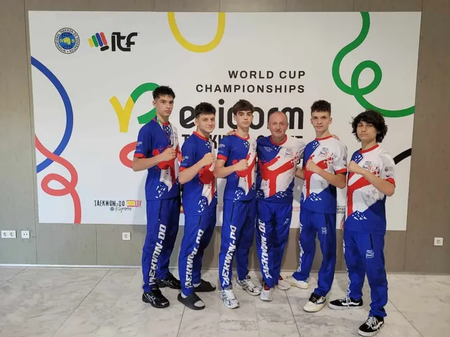 Șase tineri sportivi în echipamente sportive albastre și albe stau în linie în fața unui panou publicitar alb cu grafisme colorate.