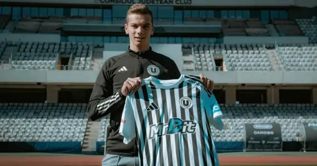 Un tânăr bărbat într-un hanorac negru ține un tricou cu dungi verticale alb-negre în fața unui stadion cu tribune goale.