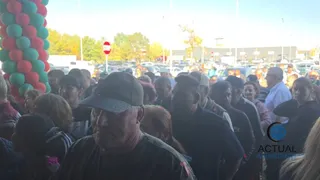 O mulțime de oameni stă strâns într-un spațiu deschis lângă o coloană de baloane verzi și roșii sub un cer luminos.