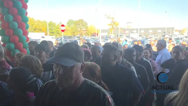 O mulțime de oameni stă strâns într-un spațiu deschis lângă o coloană de baloane verzi și roșii sub un cer luminos.