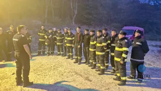 Un grup de oameni în uniforme de serviciu cu benzi reflectorizante galbene stă în linie pe un teren deschis lângă un vehicul roz.