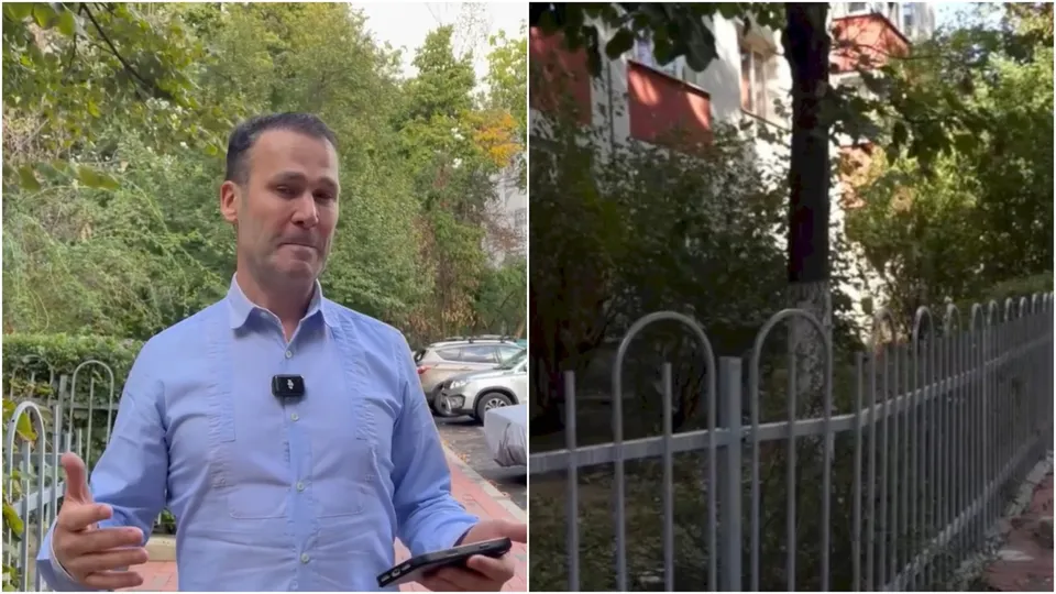 Un bărbat cu cămașă albastră stă în fața unor copaci, lângă un gard metalic gri și o mașină albă parcată.