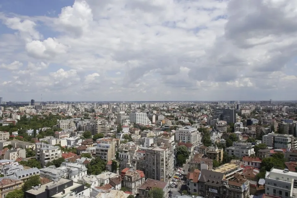 O vedere panoramică asupra unui oraș cu numeroase clădiri de diverse înălțimi sub un cer cu nori albi și cenușii.