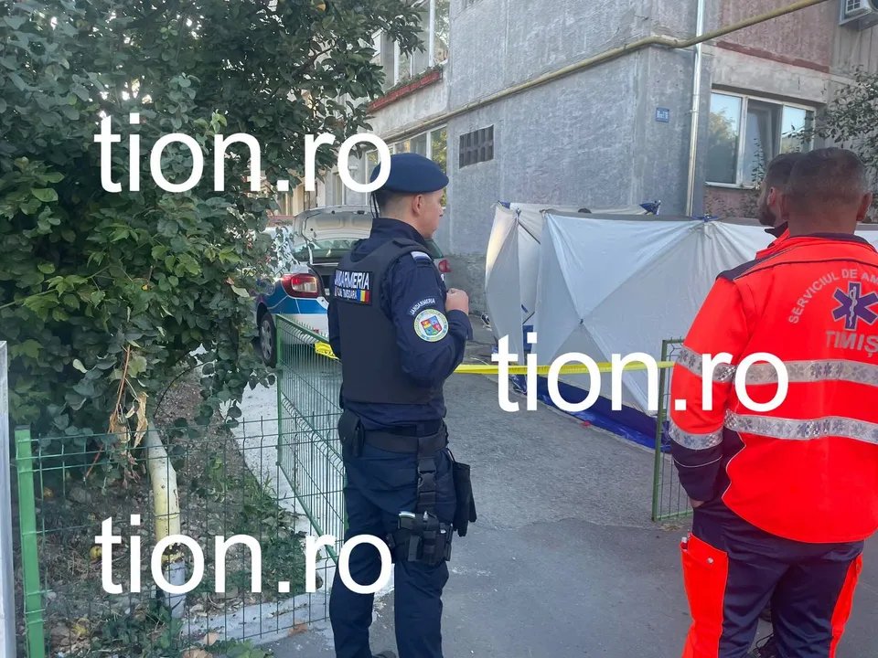 Un polițist și un salvator stau lângă un cort alb lângă un vehicul de poliție și un gard de sârmă.
