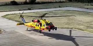 Un elicopter galben și roșu cu marcaje de serviciu medical aterizează pe o pistă de beton lângă o zonă de iarbă.