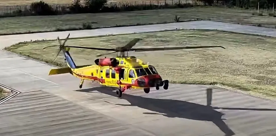 Un elicopter galben și roșu cu marcaje de serviciu medical aterizează pe o pistă de beton lângă o zonă de iarbă.
