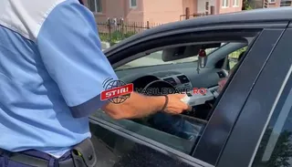 Un agent în uniformă albastră ține un aparat de testare în fața geamului deschis al unei mașini negre.