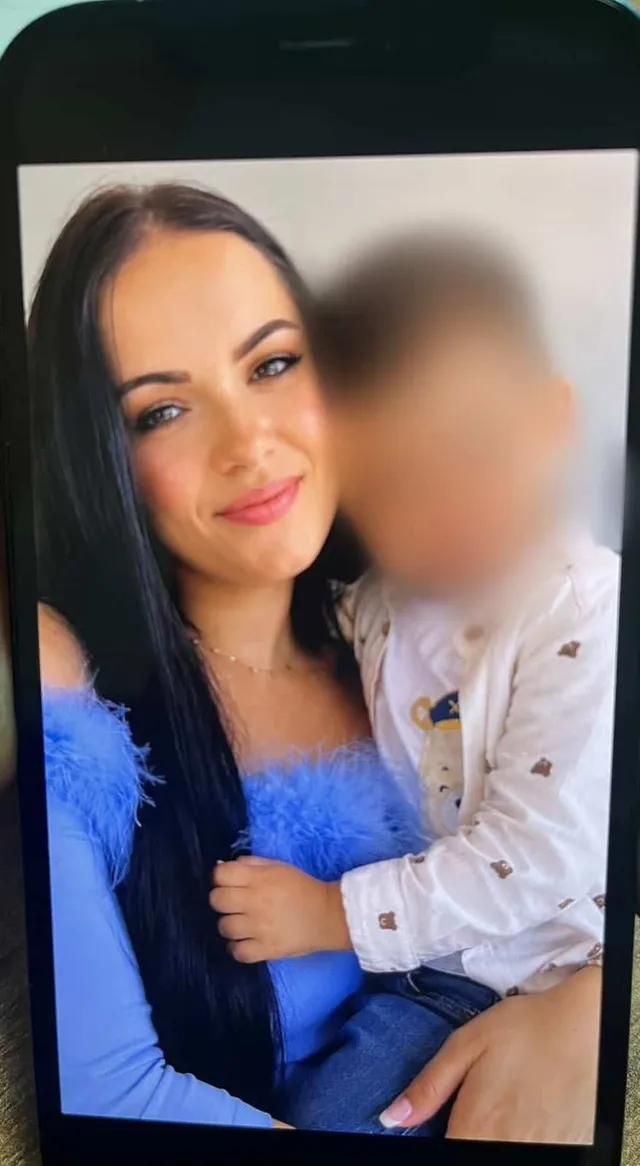 O femeie cu părul negru și un copil cu fața blurată sunt prezente într-o fotografie afișată pe un ecran de telefon mobil.