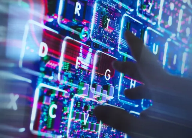 O mână întinde degetele spre tastele unui tastatură iluminată de lumini colorate și circuite electronice vizibile sub suprafața transparentă.