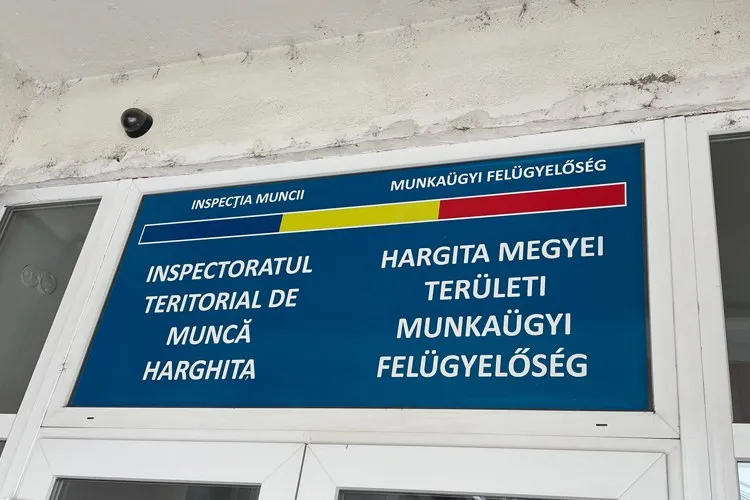 Un panou albastru cu text alb și culori galben și roșu este montat deasupra unei uși albe.