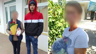 Un bărbat cu o jachetă roșie, neagră și albă stă lângă o femeie cu vestă albastră care ține un buchet de flori și o pungă.