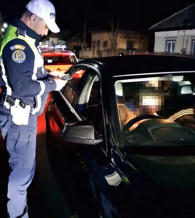 Un polițist în uniformă stă lângă o mașină neagră și scrie pe o foaie de hârtie sub lumină nocturnă.