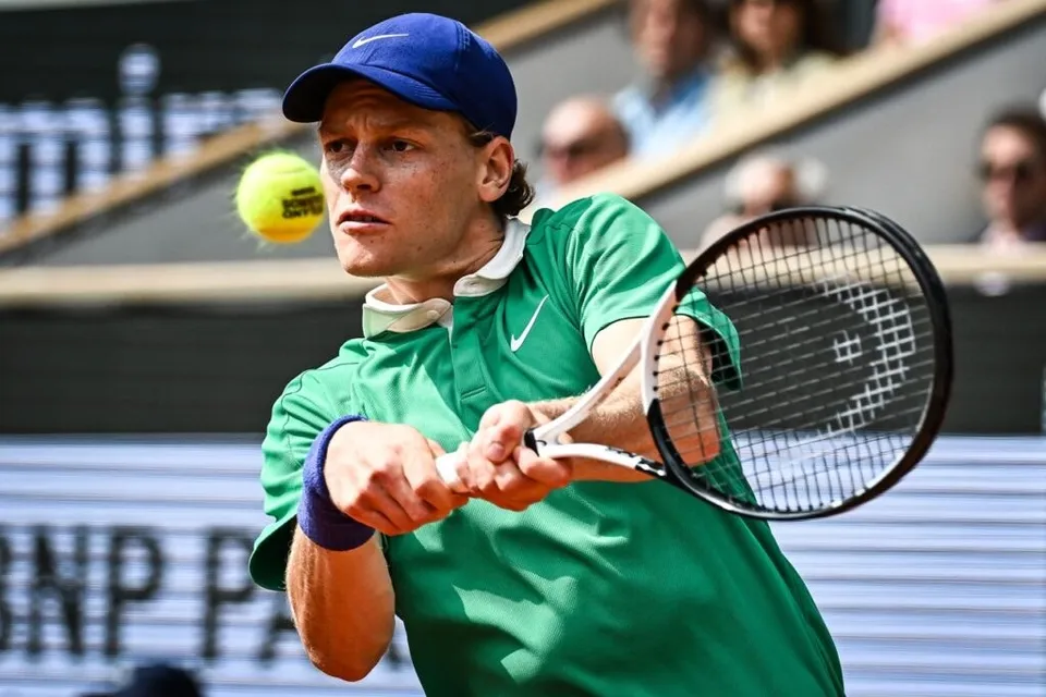 Un jucător de tenis cu șapcă albastră și tricou verde lovește o minge galbenă cu o rachetă de tenis.